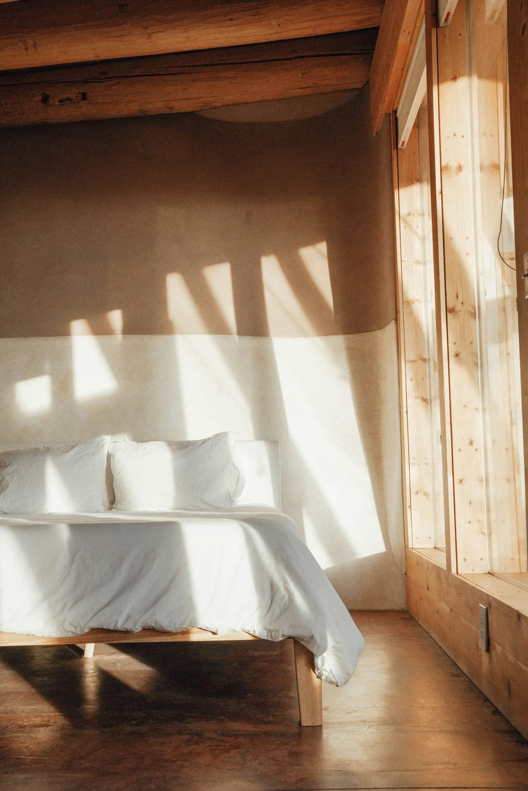 Frisch bezogenes Bett in einem Holzzimmer, Morgenlicht durch das Fenster